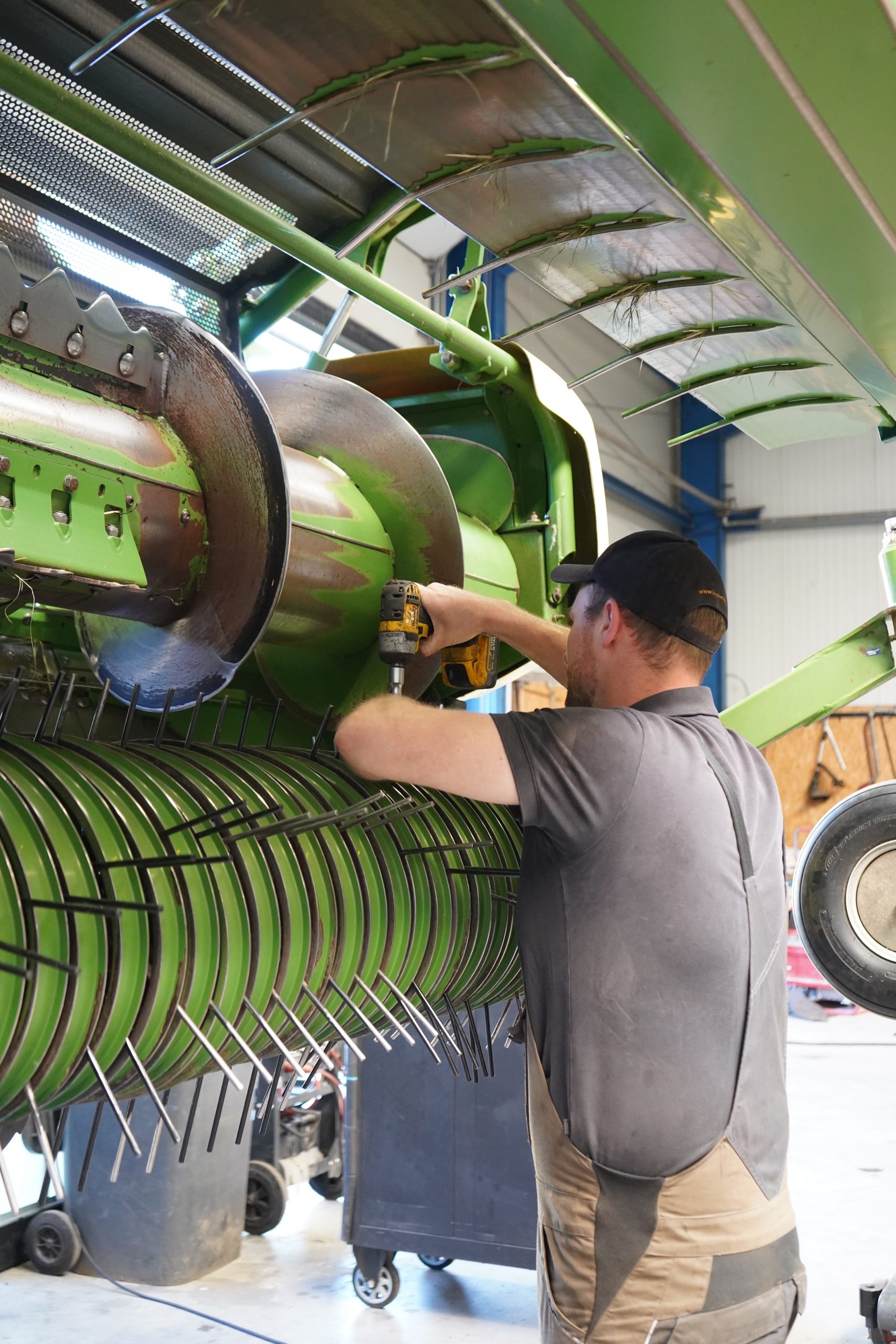 Mitarbeiter arbeitet mit Akkuschrauber an der grünen Pickup-Einheit einer landwirtschaftlichen Maschine.