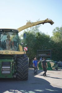 Zwei Mitarbeiter stehen vor einem großen Krone-Feldhäcksler mit aufgerichtetem Auswurfbogen auf dem Betriebshof.