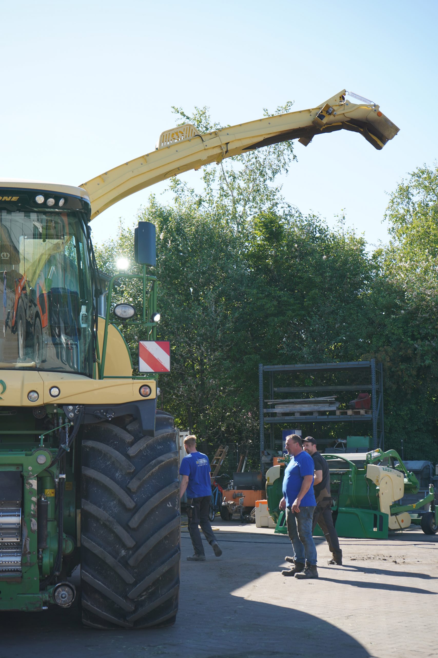 Drei Mitarbeiter des Lohnbetriebs Bohmann stehen neben einem Krone-Feldhäcksler auf dem Betriebshof.